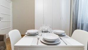A dining table set with plates, glasses, and cutlery, with white chairs and a door in the background. - Italianway Easy - Sacconi 2 A (Milan)