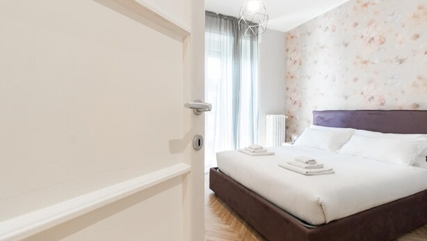 A bedroom with a bed, a nightstand, a radiator, and a window with curtains. - Italianway Easy - Sacconi 2 A (Milan)