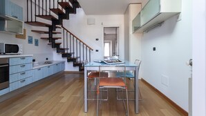 Una cocina moderna con una escalera de madera, un comedor con mesa de vidrio y una isla de cocina con microondas.