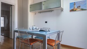 Un comedor con una mesa de vidrio, sillas de metal y un cuadro de un faro en la pared.