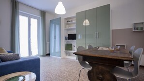 Una sala de estar moderna con un sofá, una mesa de comedor con sillas, un televisor en un estante y un armario grande.
