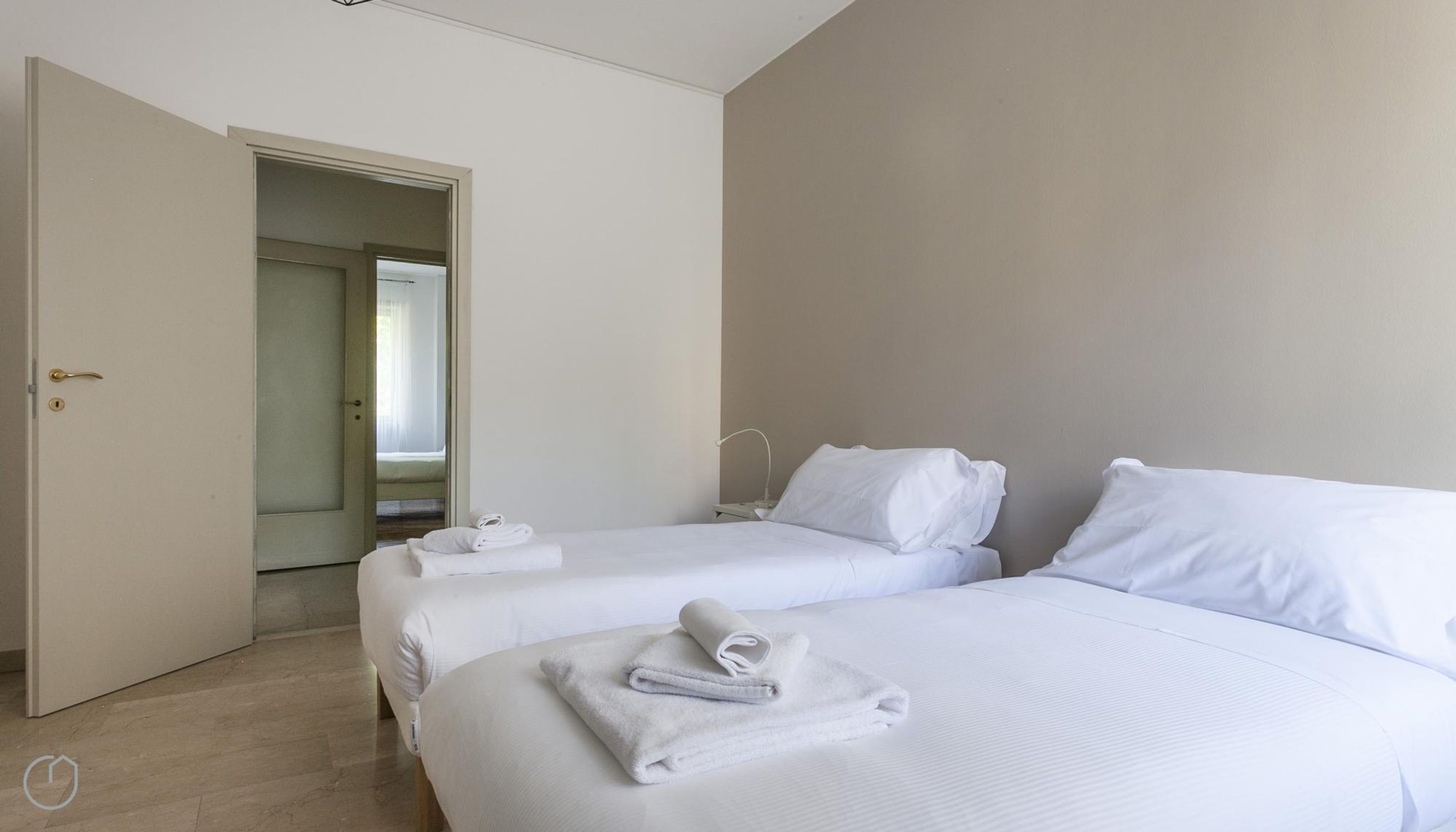 Une chambre d’hôtel avec deux lits, chacun équipé de draps et de serviettes blancs, d’une table de chevet et d’une porte donnant sur une autre pièce.