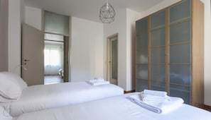 Habitación de hotel con dos camas, un armario con puertas de cristal satinado y una lámpara colgante de diseño geométrico.
