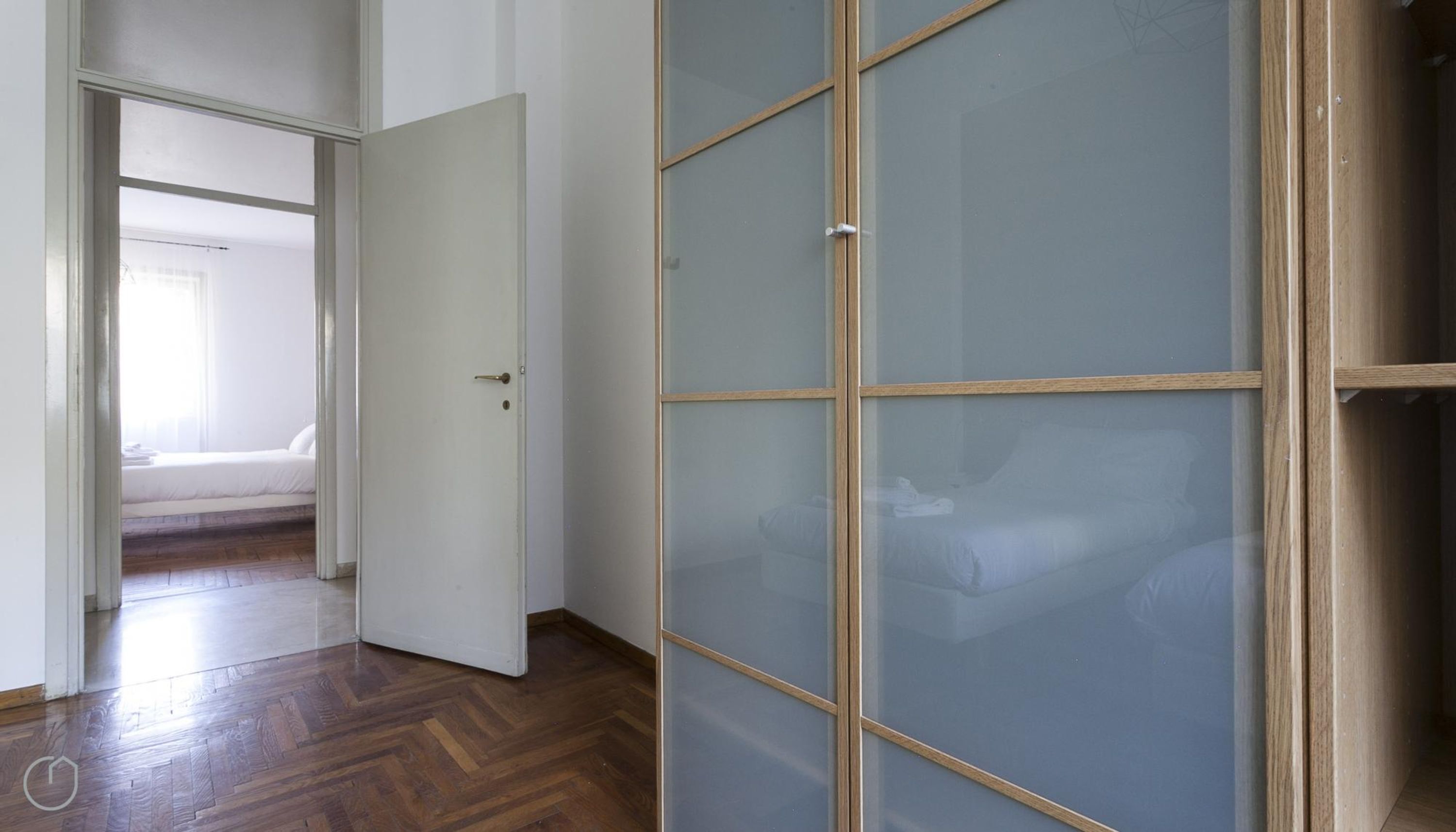 A room with a wooden herringbone floor, a white door, and a glass partition with a wooden frame.