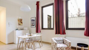 A modern living room with a dining area, large windows with red curtains, a white sofa, and a white cabinet. - Bergonzoli Place (Milan)