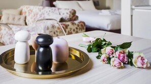 Une chambre d’hôtel avec un lit, une table de chevet sur laquelle se trouvent des salières et des poivrières, ainsi qu’un bouquet de roses.