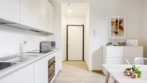 A modern kitchen with a built-in oven, microwave, and stainless steel range hood. There is a dining area with a table and chairs, and a small cabinet with a microwave and a bowl. - Bergonzoli Place (Milan)