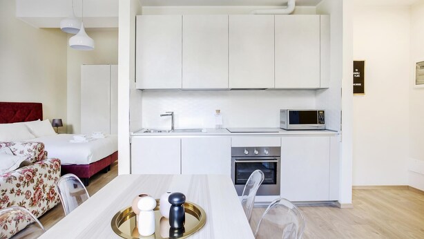 A compact hotel room with a bed, a small kitchenette with a microwave, a sink, and a stove. - Bergonzoli Place (Milan)