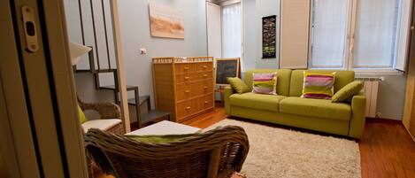 A compact living space with a green sofa, wicker furniture, a small table, and a cabinet.