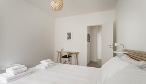 A minimalist hotel room with a bed, a desk, a chair, and a bathroom. - Sebastiano Veniero 8 (Milan)