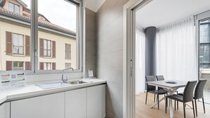 Een moderne keuken met een groot raam, een eethoek met een tafel en stoelen, en uitzicht op omliggende gebouwen.