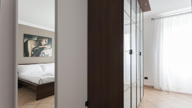 Een moderne slaapkamer met een bed, een schilderij aan de muur en een schuifdeur naar een balkon.