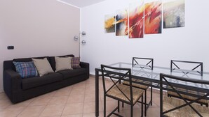 Een moderne woonkamer met een zwarte bank, een glazen eettafel en drie abstracte schilderijen aan de muur.