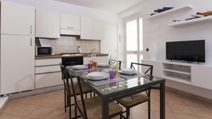Een moderne keuken met witte kasten, een magnetron, fornuis en een eethoek met een glazen tafel en stoelen.