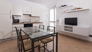 Een moderne keuken met witte kasten, een magnetron, fornuis en een eethoek met een glazen tafel en stoelen.