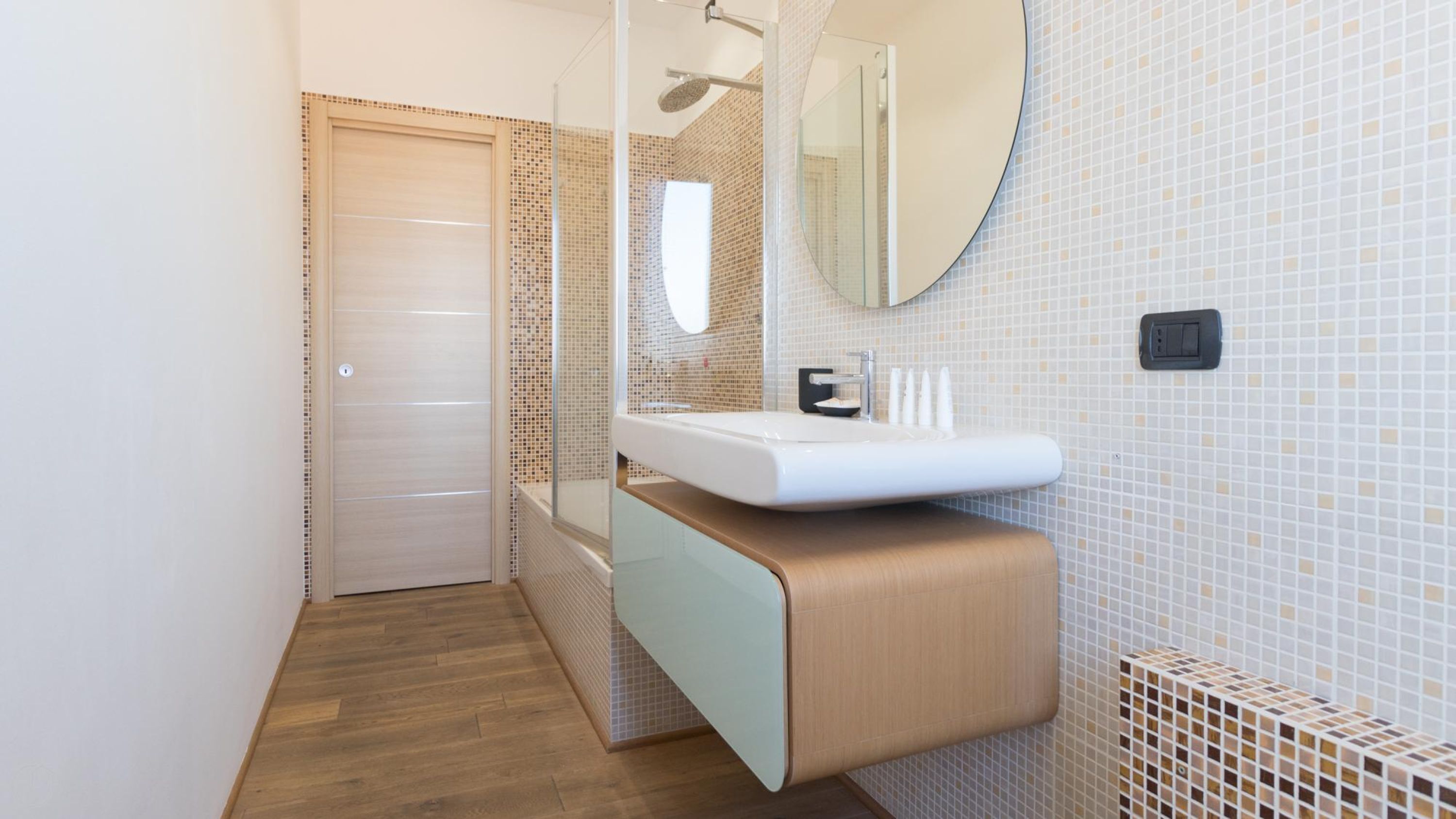 A modern bathroom with a wooden floor, a white sink, and a glass shower enclosure.