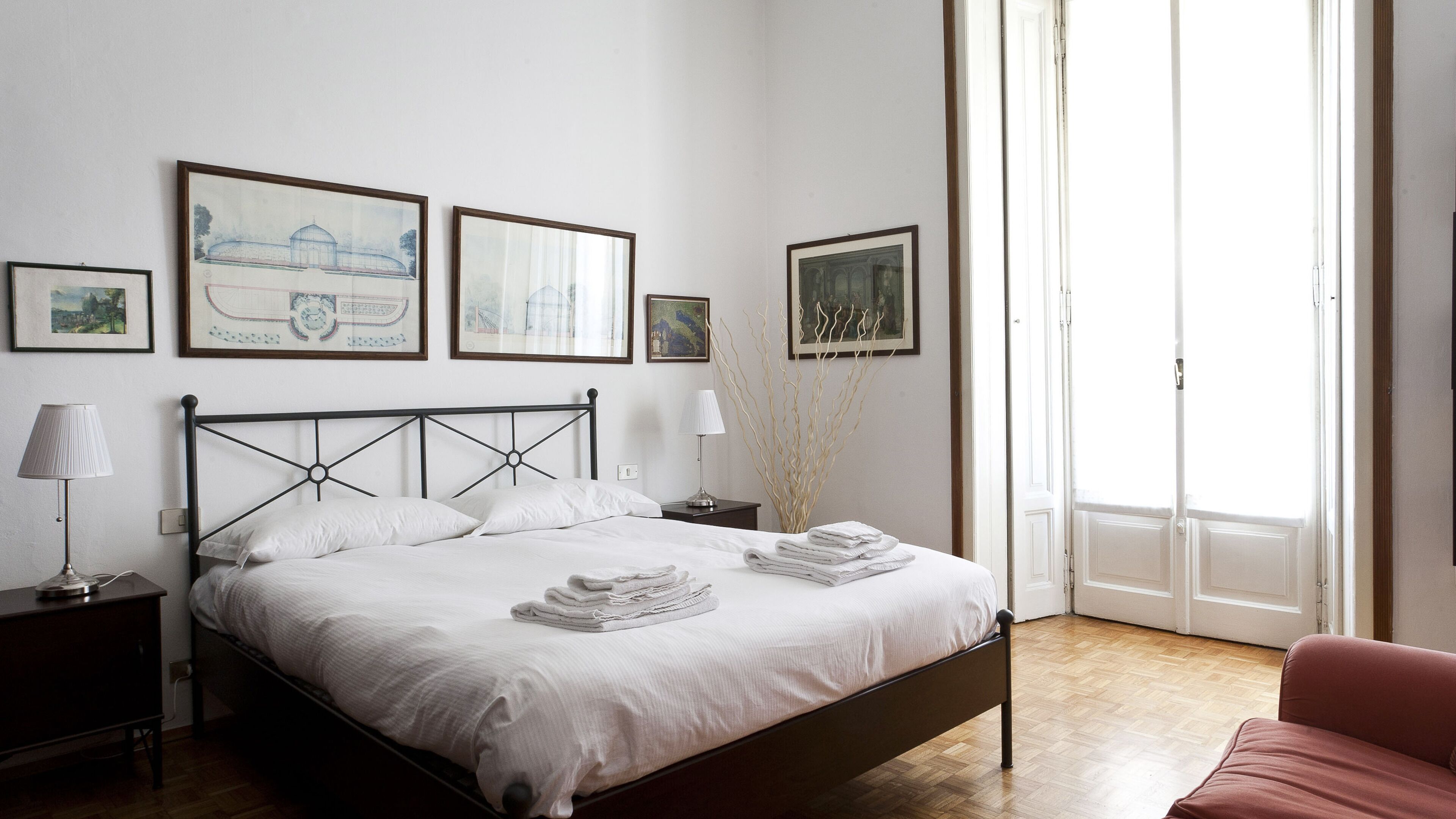 A neatly made bed with white linens and towels, a bedside lamp, and a nightstand. There are three framed artworks on the wall above the bed.