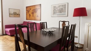 A dining area with a wooden table, six chairs, a red floor lamp, and a world map painting on the wall.
