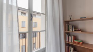 A room with a large window, a bookshelf, and a view of a building outside.
