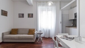 A modern living room with a sofa, a dining table, and a kitchen area.