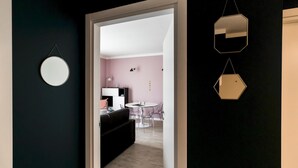 A hallway leading to a room with a round mirror, a hexagonal mirror, and a dining area with a pink wall and a black couch. - Italianway Comfort - Buenos Aires 65 A (Milan)
