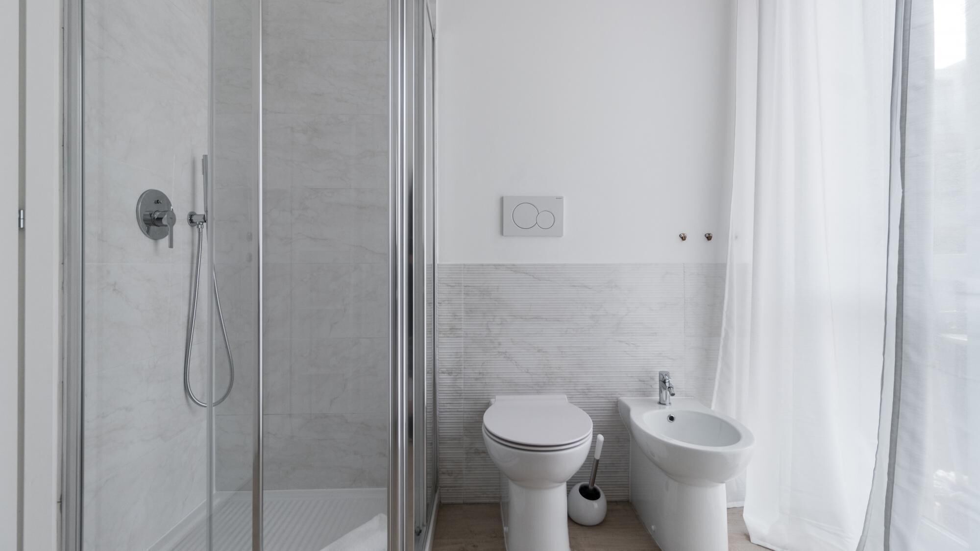 A modern bathroom with a glass-enclosed shower, a toilet, a bidet, and a sink.