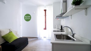 A modern kitchen with a built-in sink, a toaster, and a kettle. There is a green pillow on a black sofa in the living area. A sign on the wall reads "Vico Liceti Apartments." - Liceti 5 A (Rapallo)