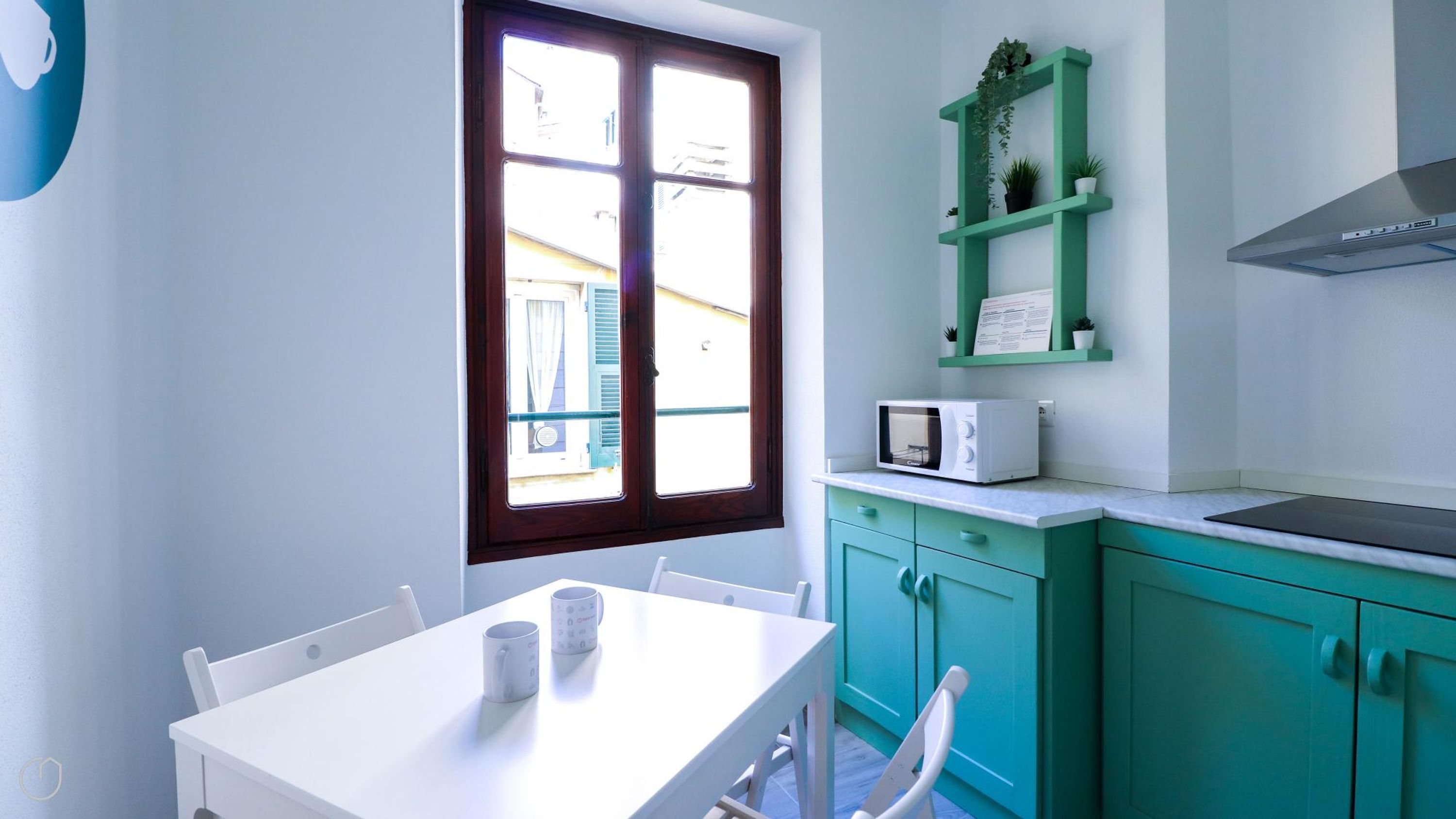 Cozinha com armários azul-turquesa, bancada branca, micro-ondas e janela com vista para edifícios.