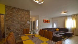 A modern living room with a stone accent wall, a dining area with yellow placemats, and a brown leather sofa.