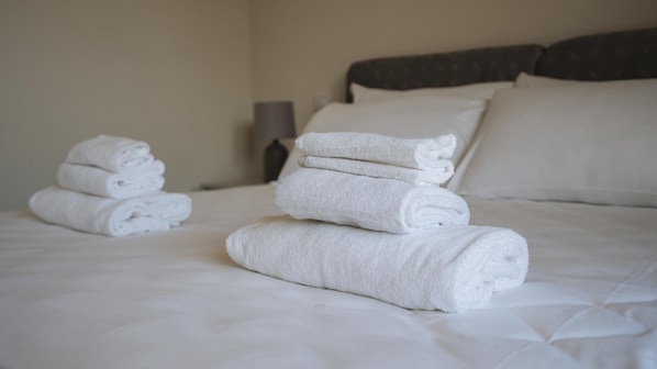 A neatly made bed with white linens and pillows, a bedside lamp, and a wall-mounted light fixture.