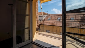 Un balcon doté d’un sol carrelé et offrant une vue sur les bâtiments voisins, dont les toits sont recouverts de tuiles rouges.