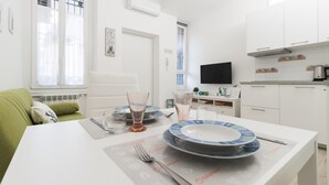 A modern kitchen with white cabinets, a dining table set with plates and glasses, a green sofa, and a flat-screen TV. - Italianway Comfort - Borsieri 25 A (Milan)