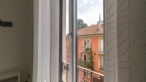 A window with white curtains, a view of a red building with balconies, and a clear sky. - Italianway Comfort - Borsieri 25 A (Milan)