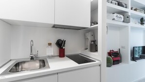 A modern kitchen with a stainless steel sink, a black induction cooktop, and white cabinetry. There are kitchen utensils in a red holder and a cactus plant on the counter. - Italianway Easy - Raffaello Sanzio 17 (Milan)