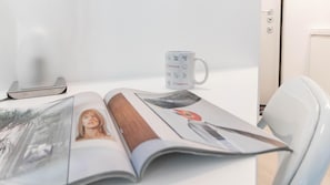 Una revista abierta sobre una mesa, con una taza de café, una bandeja y una silla.