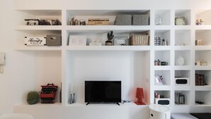 A living room with a flat-screen TV, shelves with various items, a typewriter, and a cactus. - Italianway Easy - Raffaello Sanzio 17 (Milan)