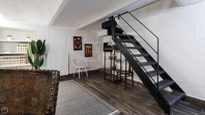 A modern living room with a wooden floor, a white chair, a small table, a black spiral staircase, and a cactus plant. - Chavez 2 (Milan)
