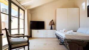 Un dormitorio con cama, televisión, escritorio con cajones, silla y ventana con persianas.