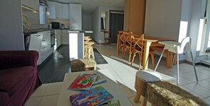 A modern kitchen with white cabinets, a dining area with wooden chairs, and a small table with children's books. - 20m from resort center, 3rd floor, balcony, tv, ski locker, 85m², Tignes (Tignes)