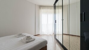 Una habitación de hotel con cama, armario de cristal y un amplio ventanal con cortinas de gasa.