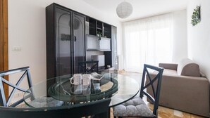 Una sala de estar moderna con una mesa de comedor de vidrio, dos sillas, un sofá y un mueble de entretenimiento negro.