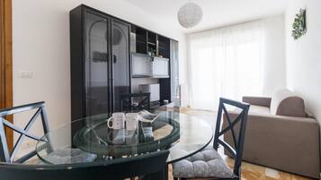 Uma sala de estar moderna com uma mesa de jantar de vidro, duas cadeiras, um sofá e um módulo de entretenimento preto.