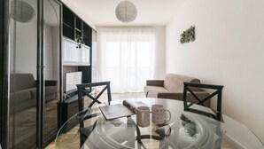 Una sala moderna con una mesa de comedor de vidrio, dos sillas, un sofá y una zona de cocina visible a través de un vidrio.