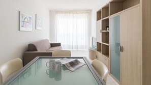 Un salon moderne avec une table basse au plateau en verre, deux fauteuils beiges, un canapé marron et une armoire en bois dotée de portes en verre.