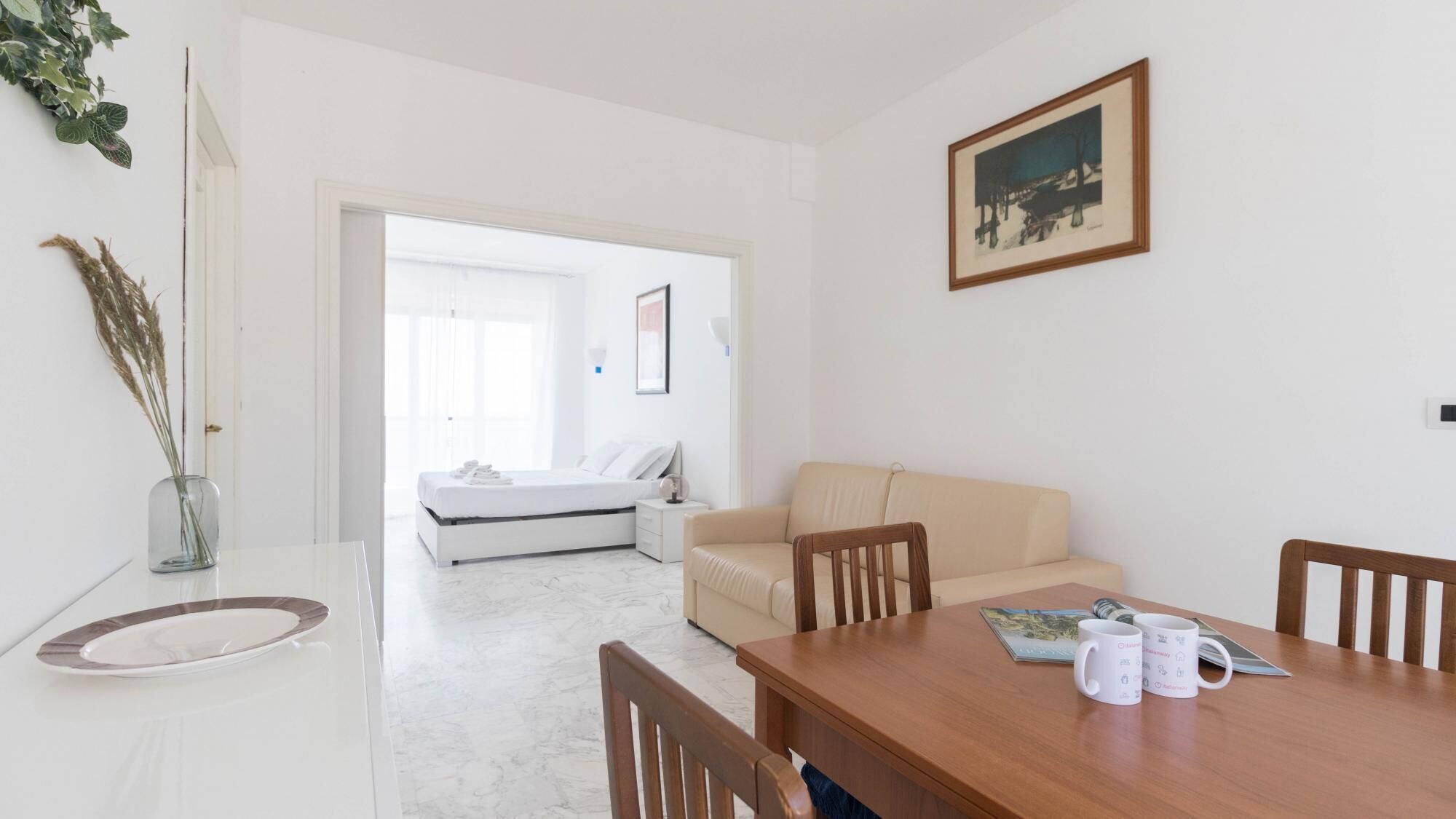 Quarto moderno e bem iluminado com uma cama, um sofá, uma mesa de jantar com cadeiras e um quadro na parede.