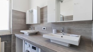 Une salle de bain moderne avec deux lavabos, un lave-linge encastré et un grand miroir.