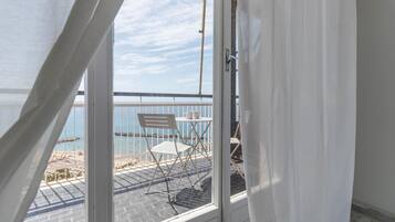 Varanda com cadeira e mesa brancas, com vista para a praia e o mar.
