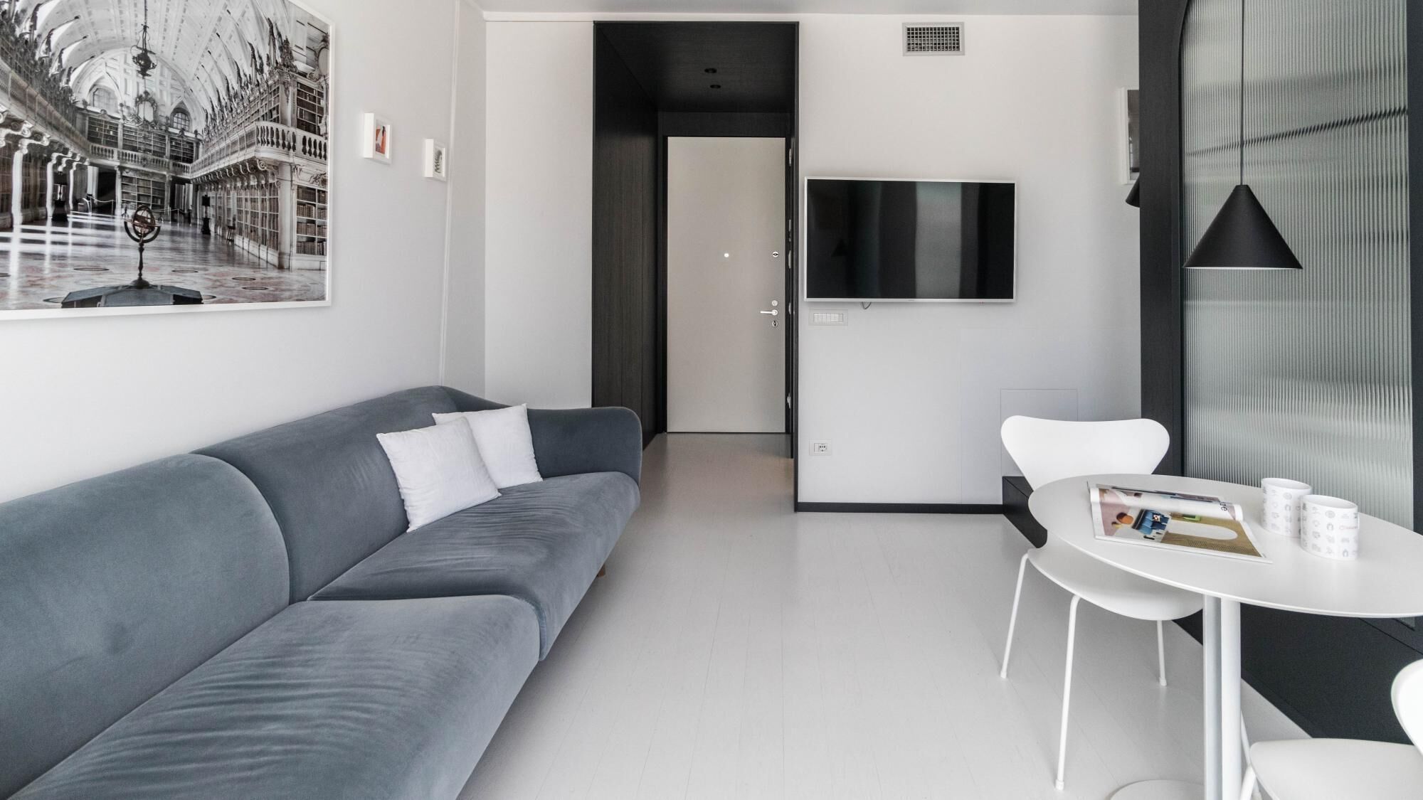 A modern, minimalist living room with a grey sofa, a white coffee table, and a TV mounted on the wall.