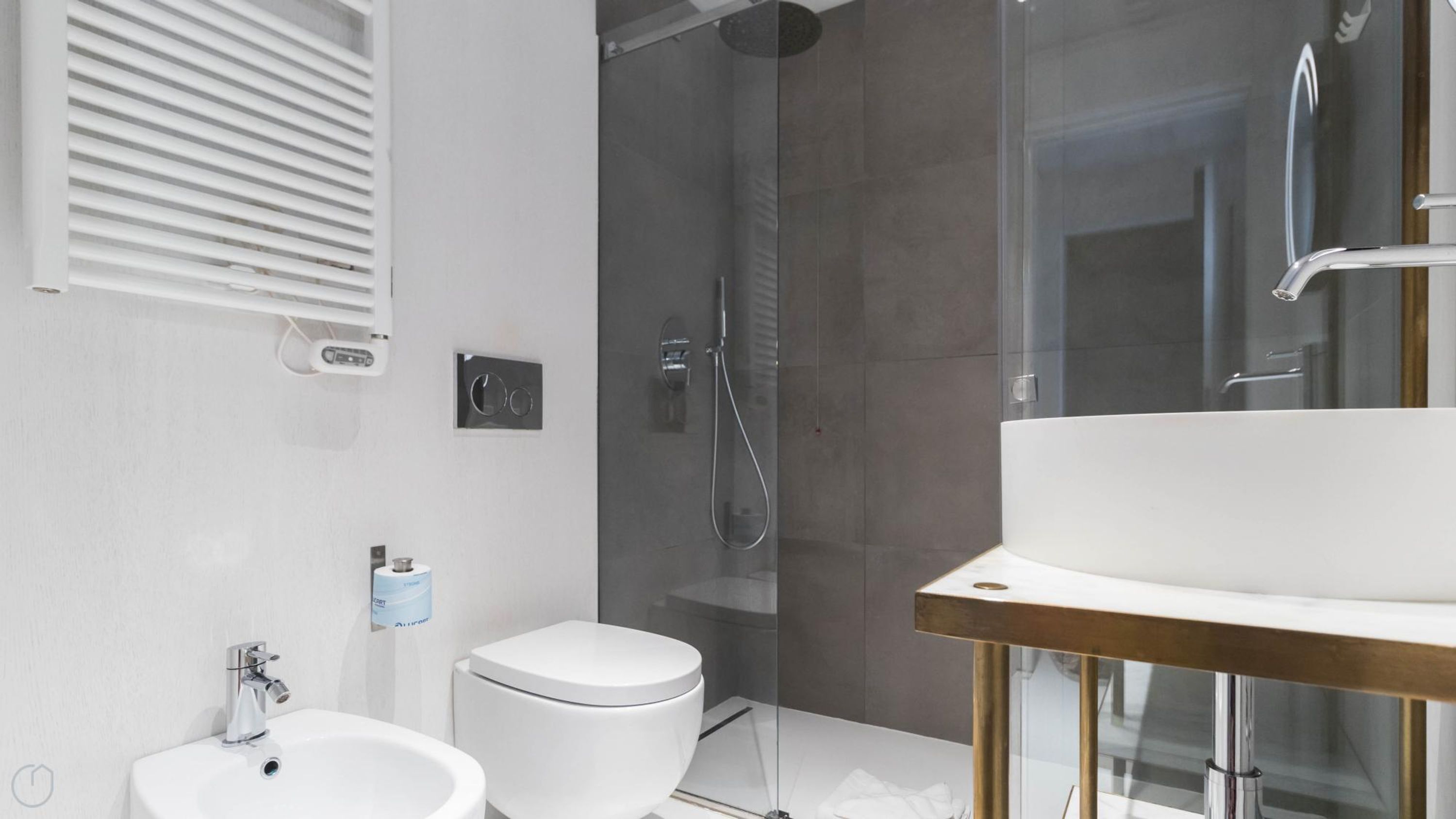 A modern bathroom with a glass shower enclosure, a white toilet, a sink, and a bidet.