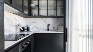 Een moderne keuken met marmeren aanrecht, een zwarte spoelbak en een koffiezetapparaat.